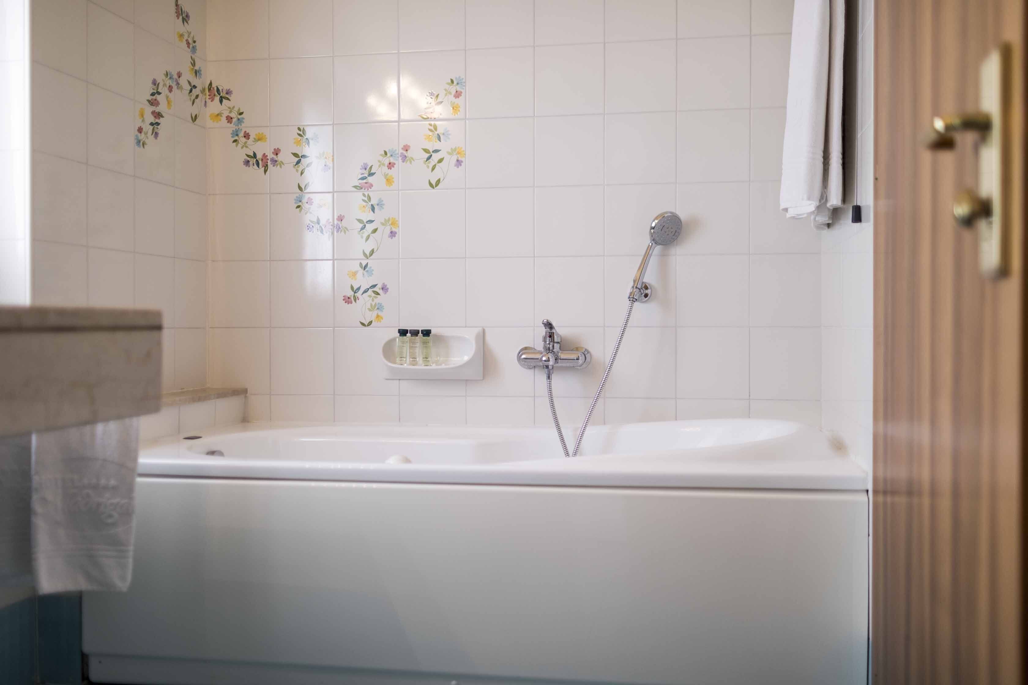 Un baño con una bañera blanca, ducha e inodoro. Hay adhesivos florales en la pared y un perchero para toallas.