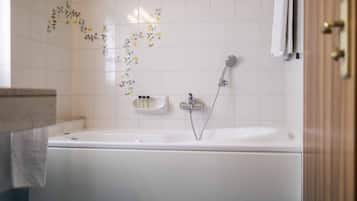 Un baño con una bañera blanca, ducha e inodoro. Hay adhesivos florales en la pared y un perchero para toallas.