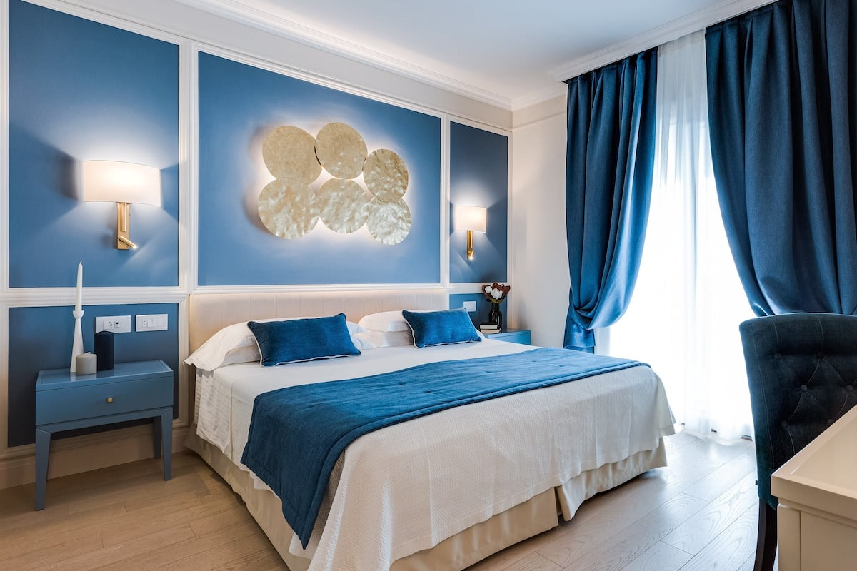 A modern hotel room with a large bed, a bedside table, a nightstand, a desk, and a chair.