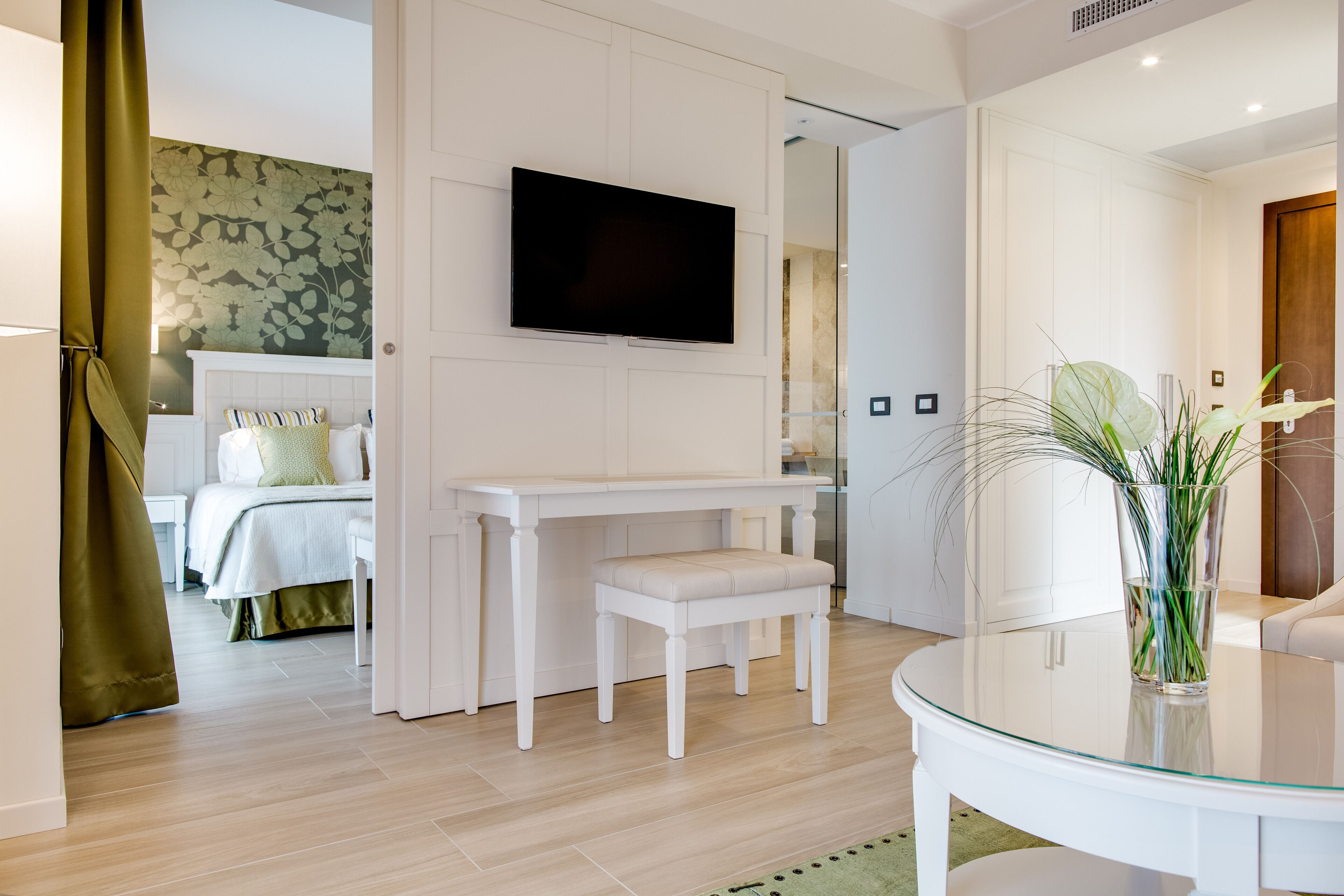 Una habitación de hotel moderna con una cama, un televisor montado en la pared, una pequeña mesa blanca y una mesa de centro de vidrio.
