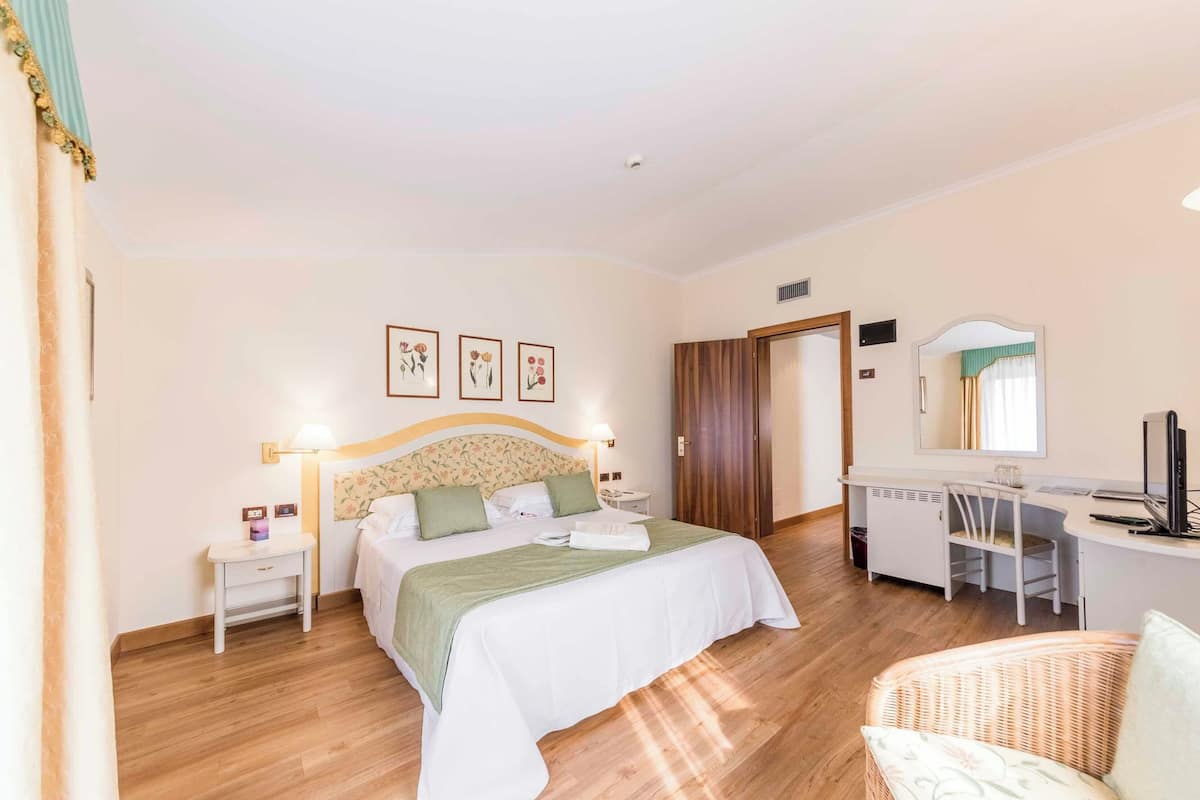 A bedroom with a bed, bedside table, desk, chair, and a mirror.