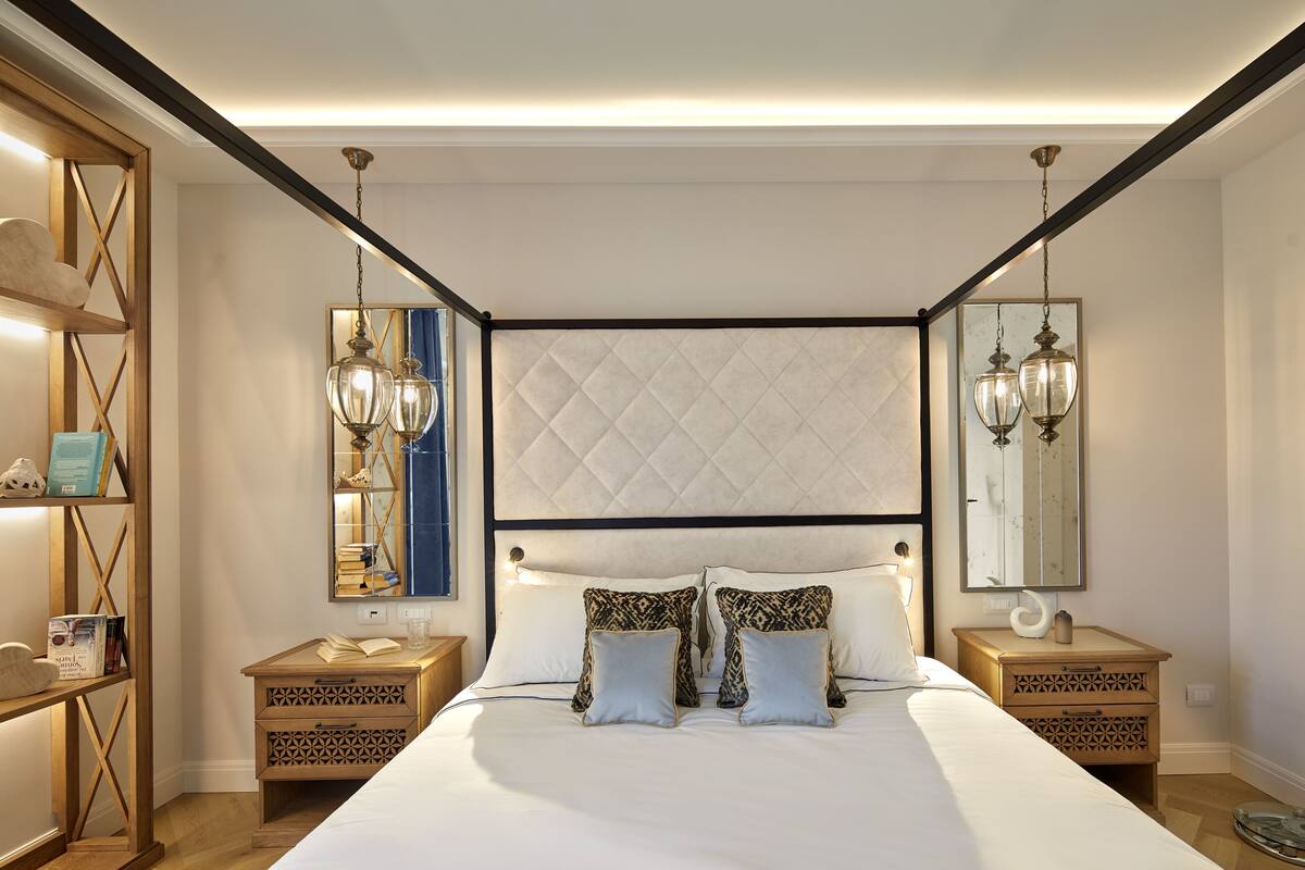 A bedroom with a large bed, two nightstands, a wooden headboard, and two wall-mounted lamps.