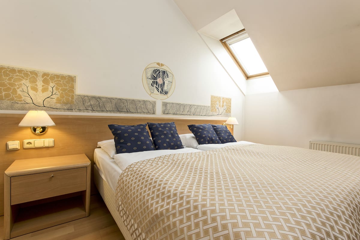 Une chambre à coucher bien aménagée, avec un grand lit, une table de chevet, une lampe fixée au mur et un puits de lumière.