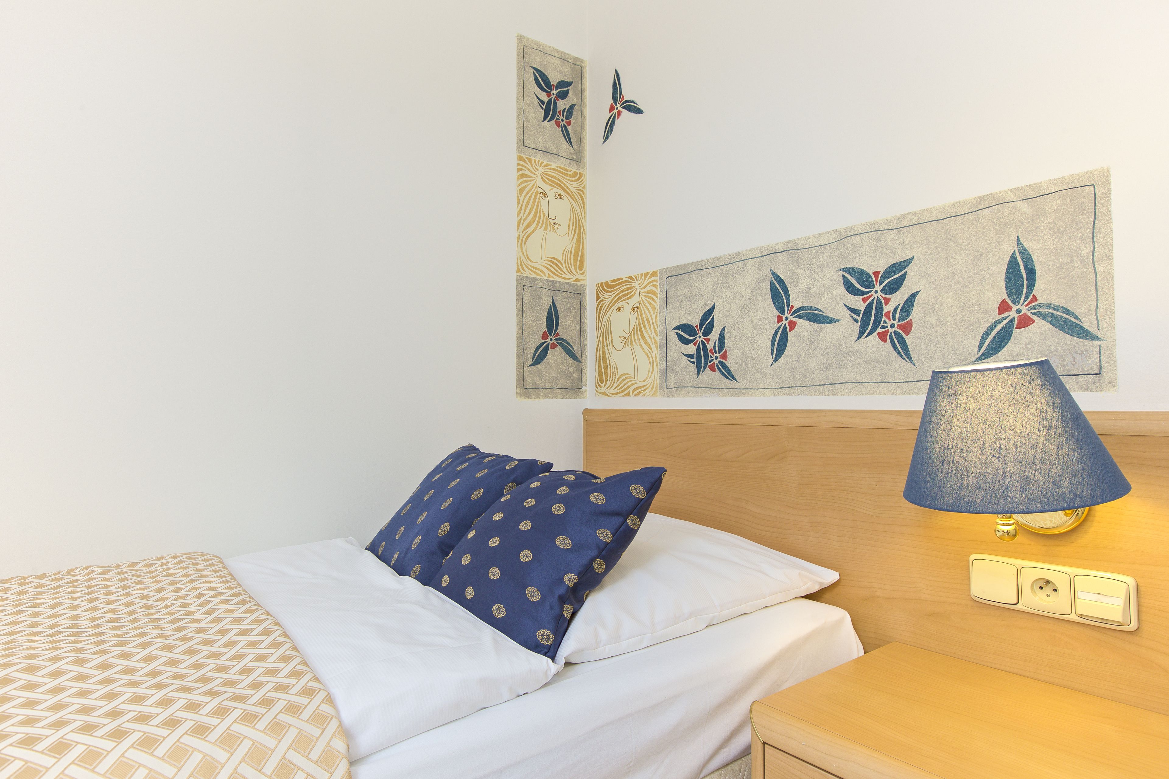 Cama bem arrumada com roupa de cama estampada, abajur de cabeceira e uma obra de arte na parede.