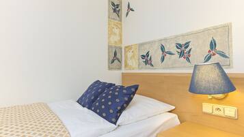 Cama bem arrumada com roupa de cama estampada, abajur de cabeceira e uma obra de arte na parede.