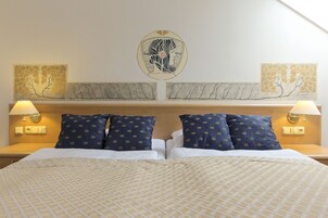 Een hotelkamer met een bed, twee wandlampen en twee kunstwerken aan de muur.