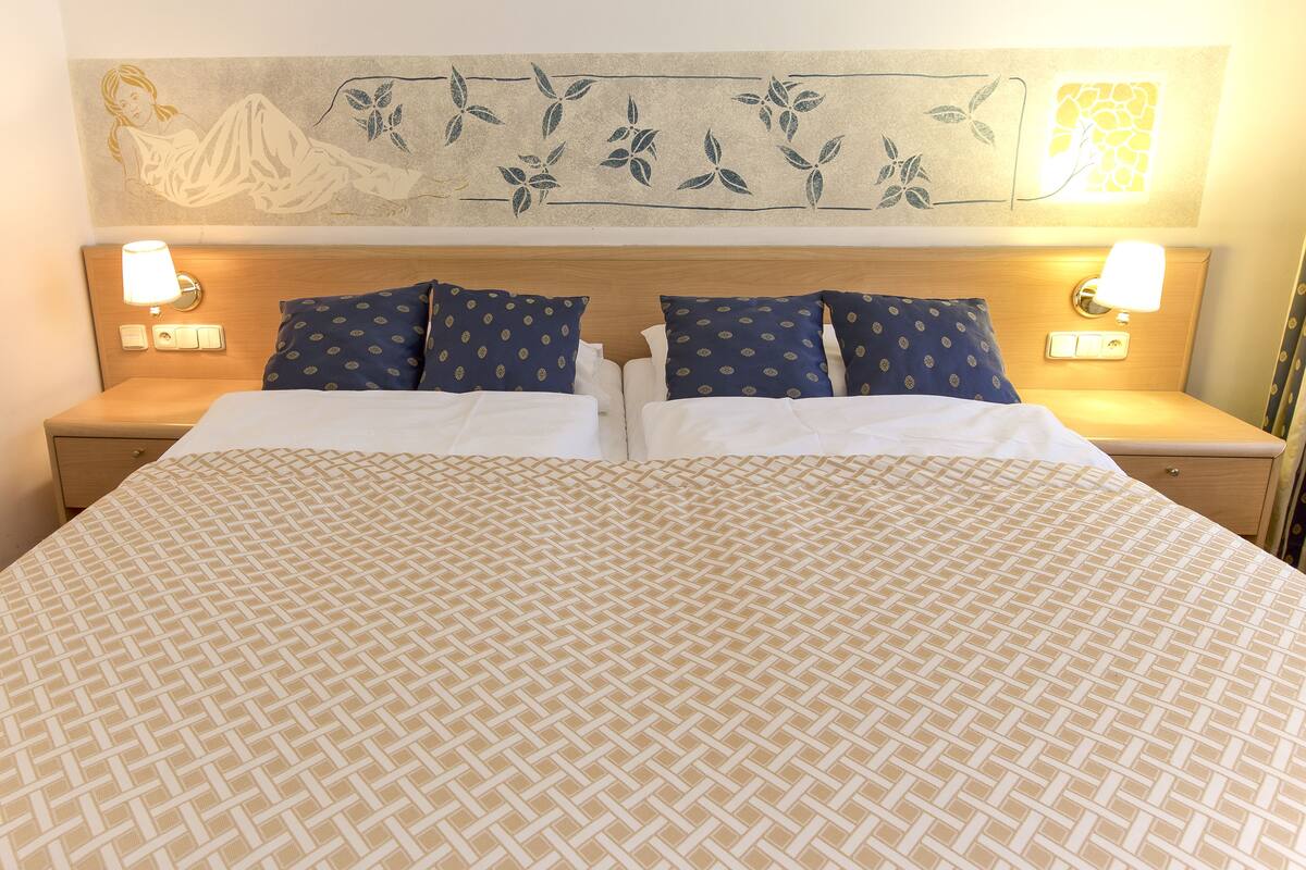 Un lit double avec une couvre-lit à motifs beige et blanc, deux oreillers assortis et deux lampes de chevet.