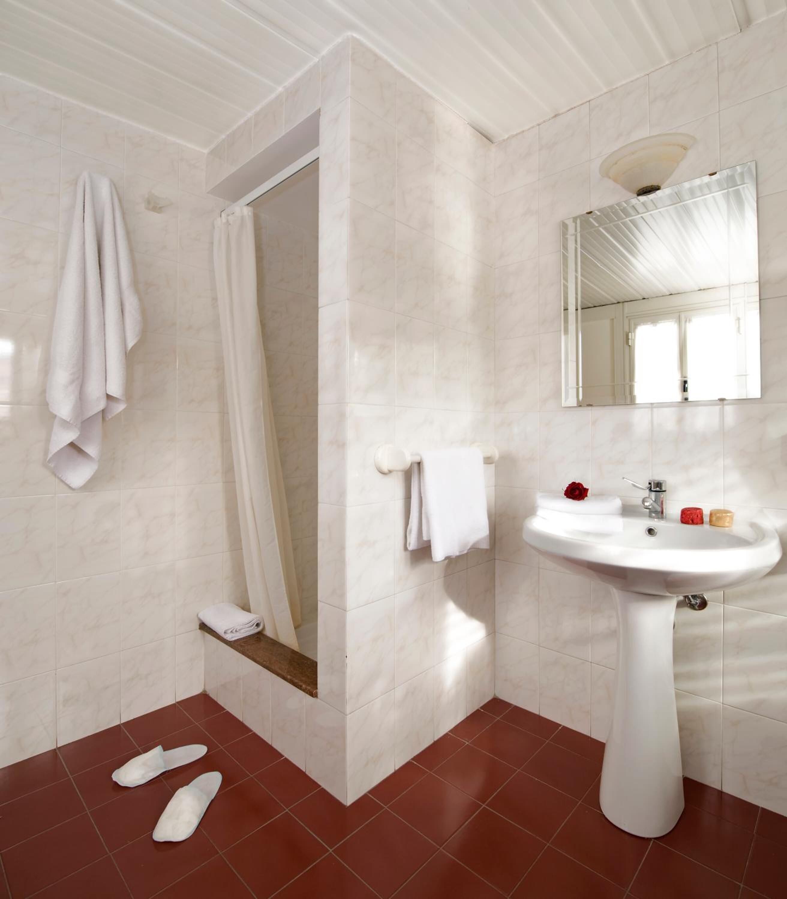 A bathroom with a white pedestal sink, a mirror, and a shower area with a white curtain.