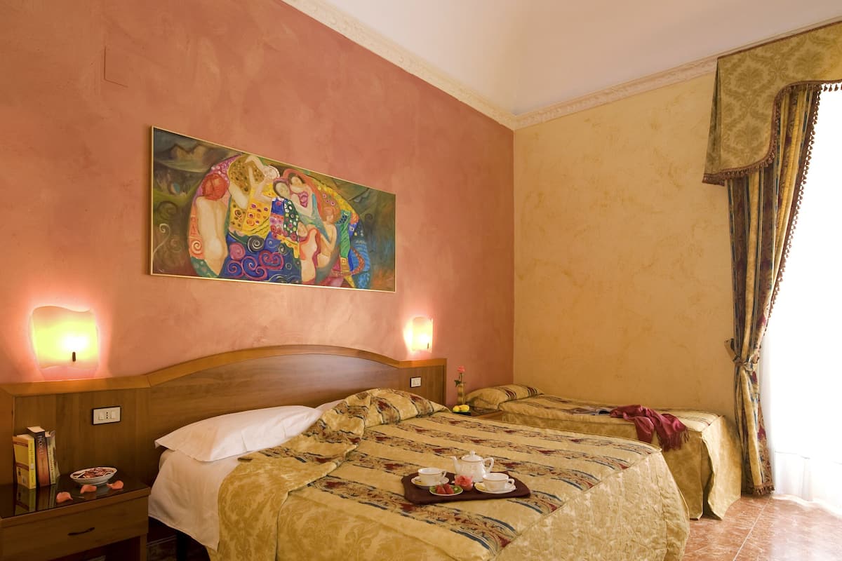 Una habitación de hotel con una cama grande, dos mesitas de noche, una lámpara de noche y un cuadro en la pared, además de una luz en el techo.