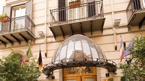 La entrada del Hotel Joli, con un llamativo letrero rojo, un toldo de cristal y plantas en macetas.