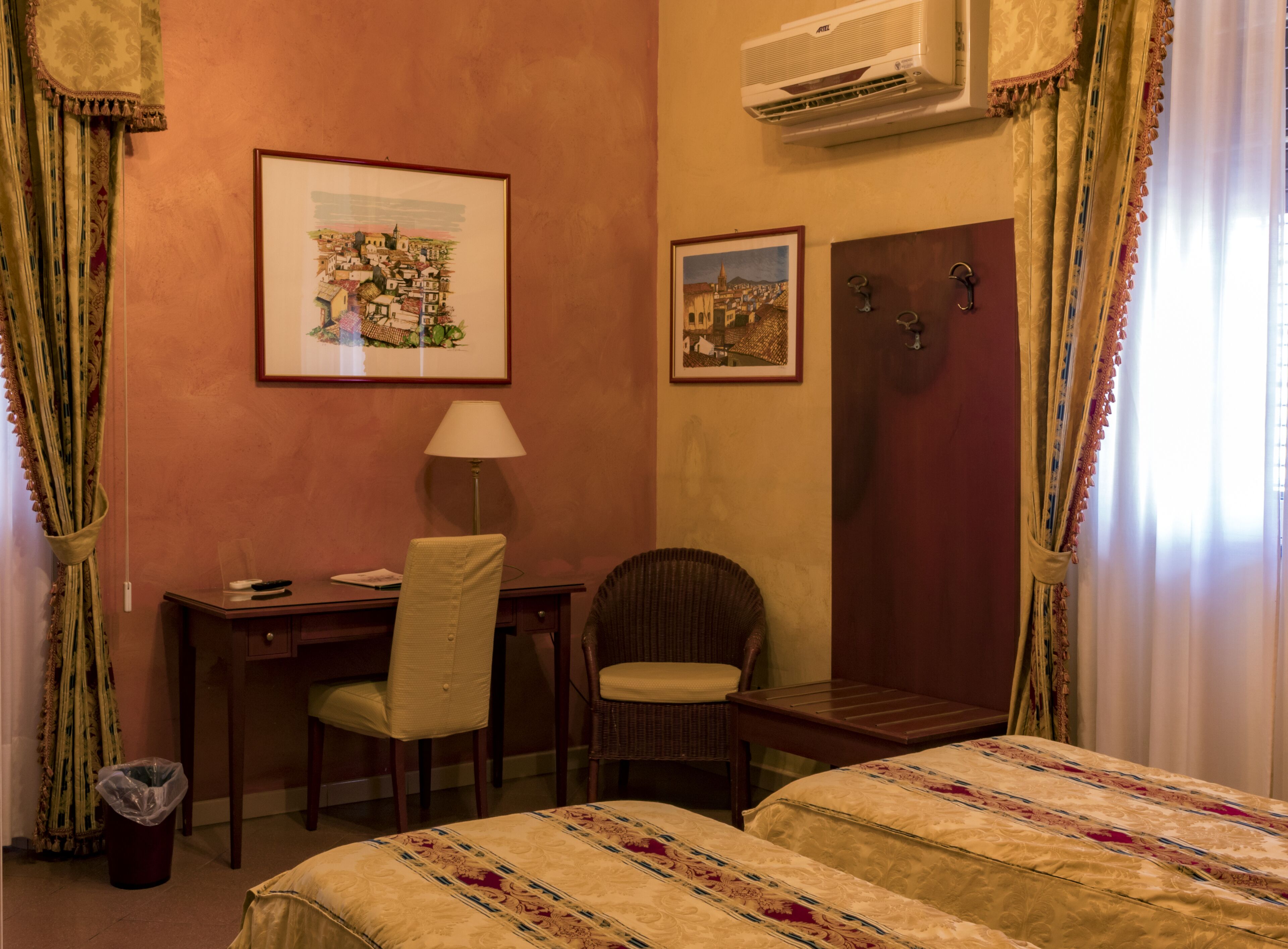 Habitación de hotel con dos camas, un escritorio con silla, una lámpara y dos cuadros en la pared.