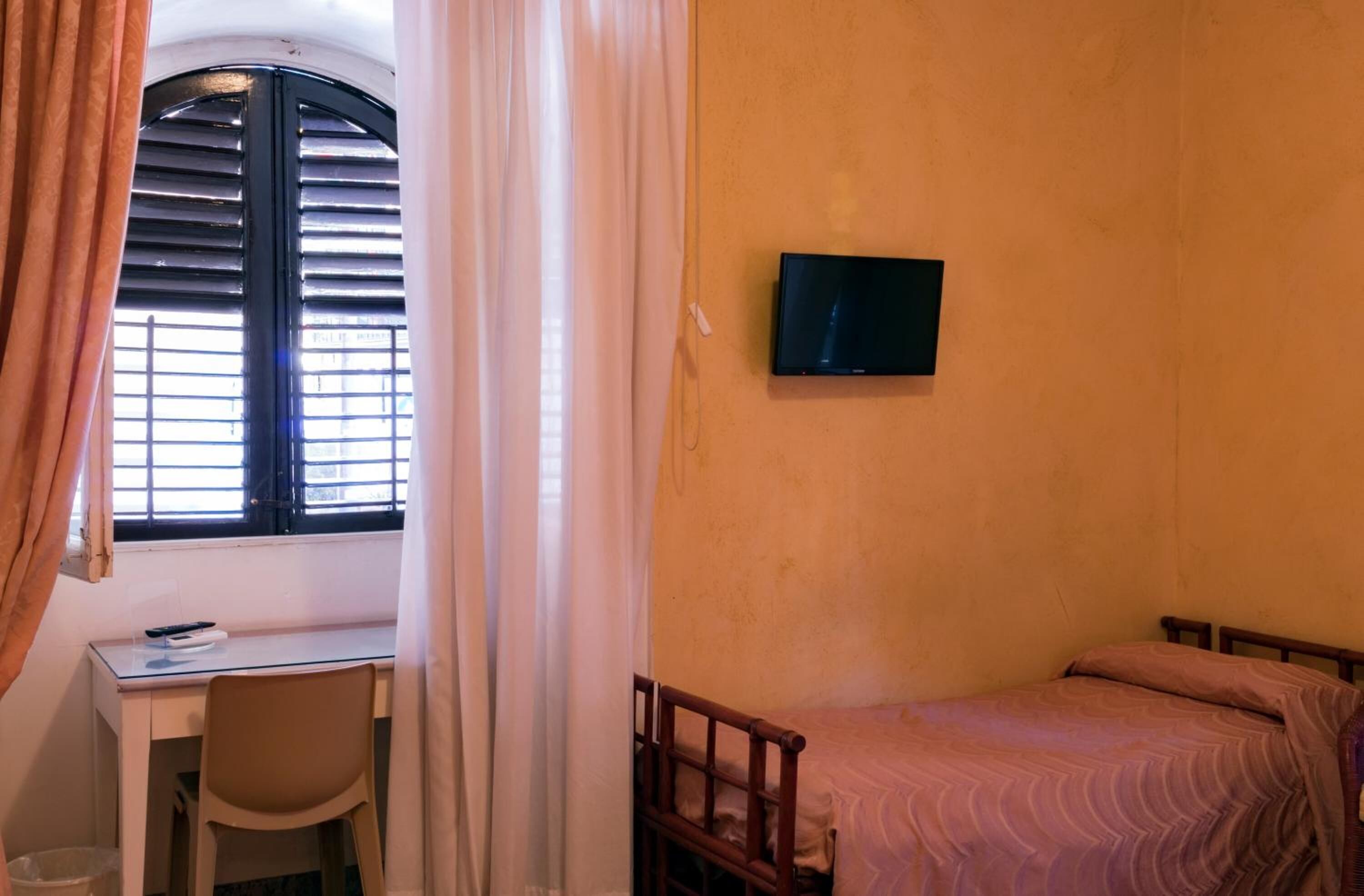 A small room with a bed, a desk, and a TV mounted on the wall.