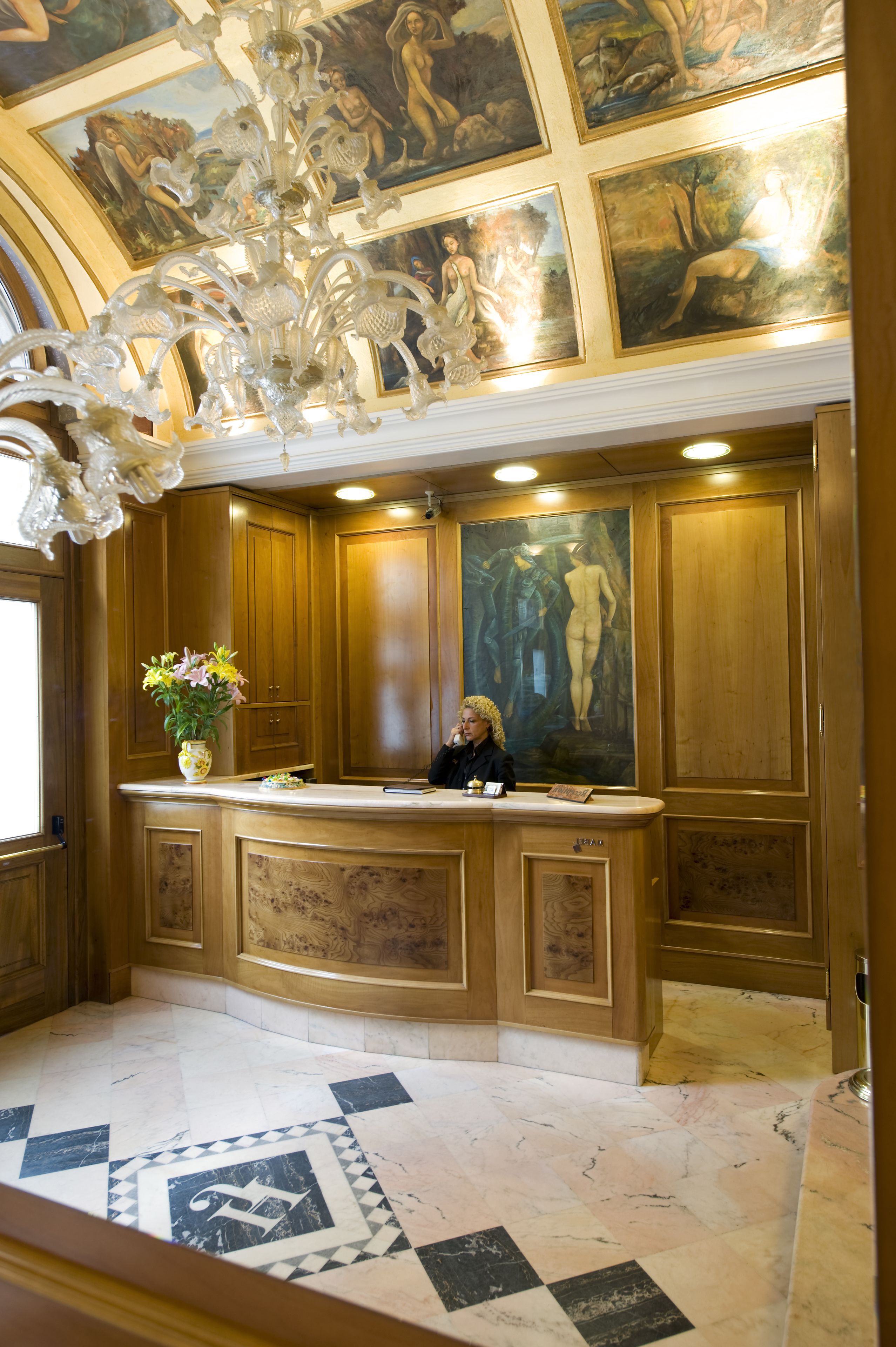 A reception area with a marble floor, wooden paneling, a chandelier, and a painting of a nude figure.