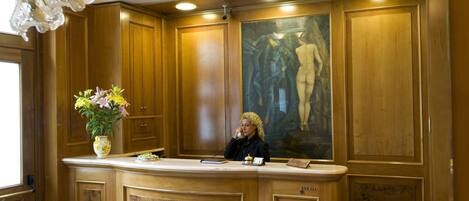A reception area with a marble floor, wooden paneling, a chandelier, and a painting of a nude figure.