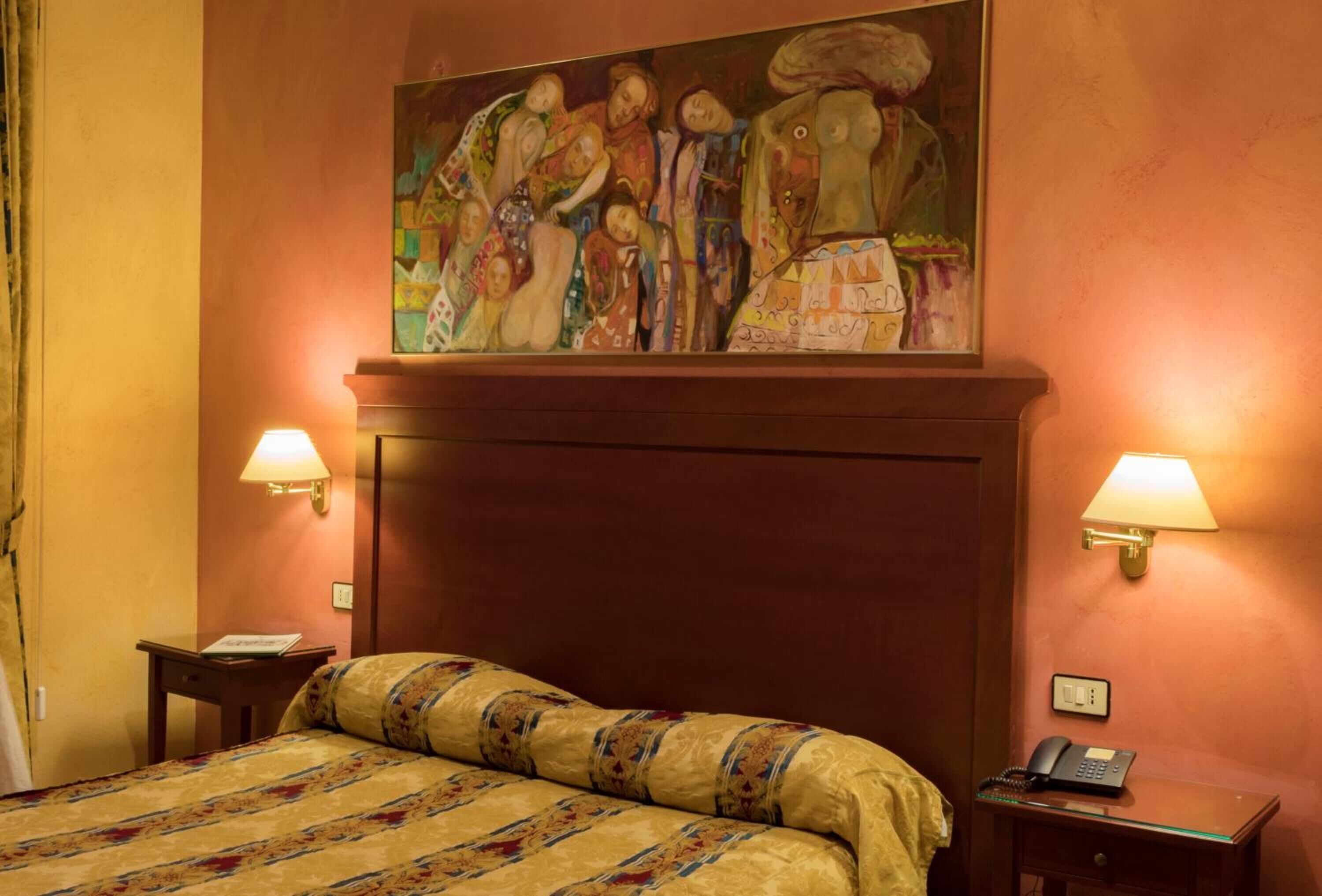 Camera d'albergo con un letto grande, due comodini, un quadro sopra il letto e due lampade a parete.