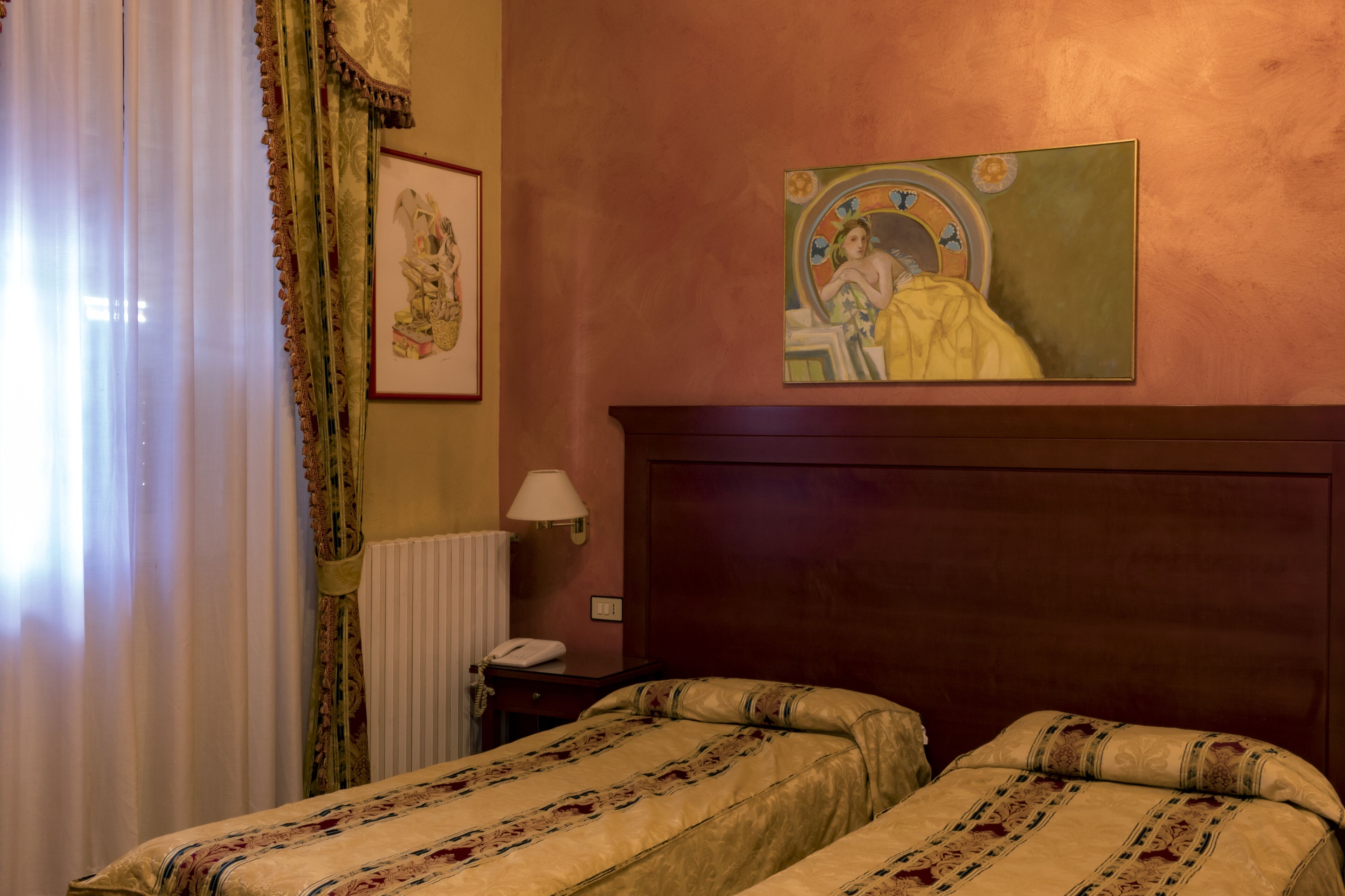 Habitación de hotel con dos camas, cabecero de madera, un cuadro en la pared, una lámpara y un teléfono en una mesita de noche.