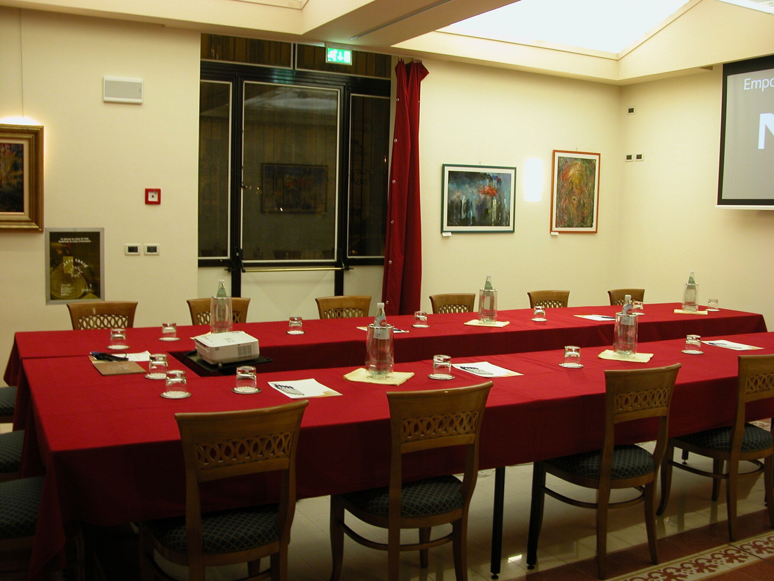 Un salón de conferencias con una mesa larga, sillas, un proyector y una pantalla.