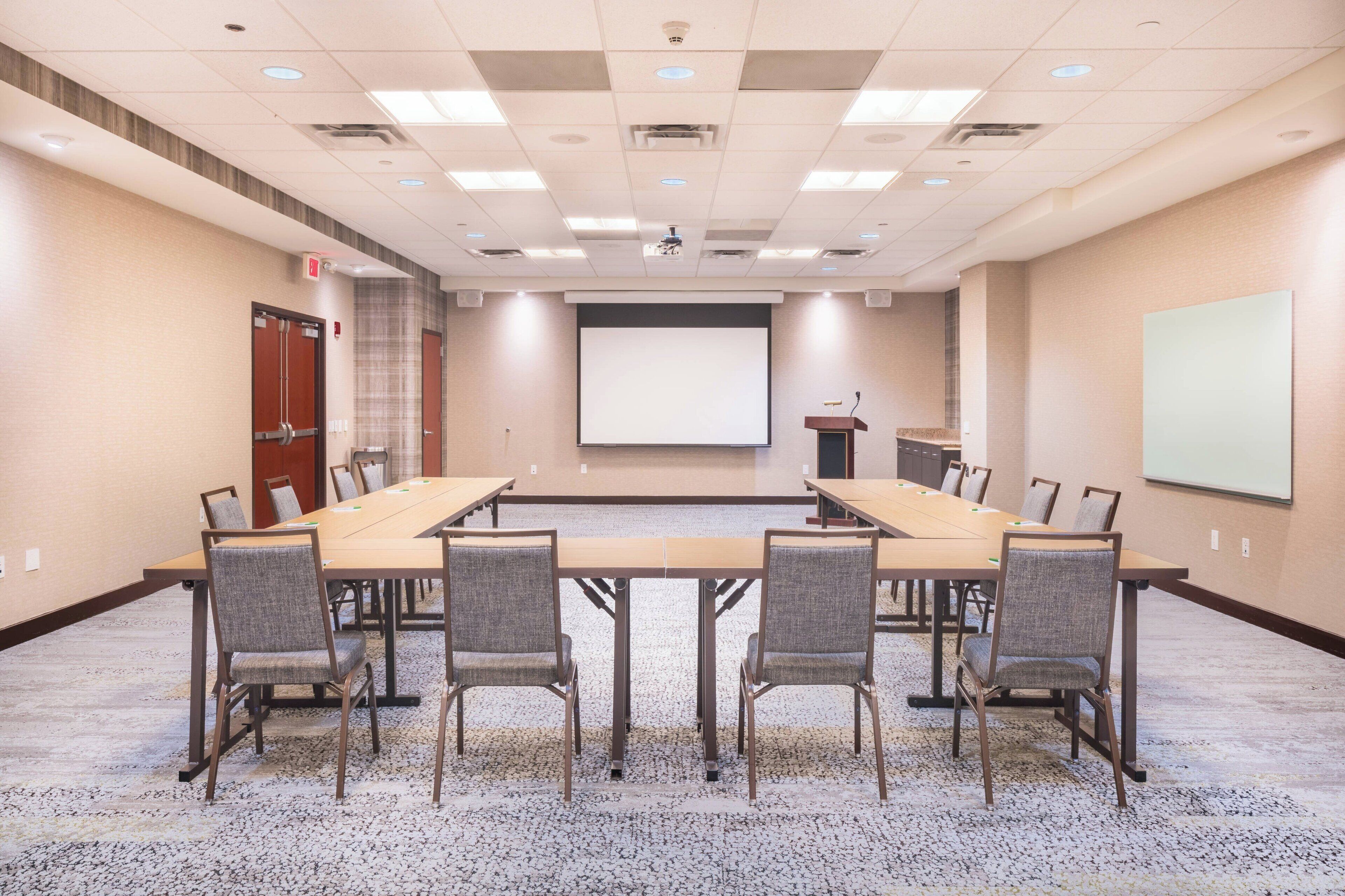 A conference room with a large table, chairs, a projector screen, and a podium.