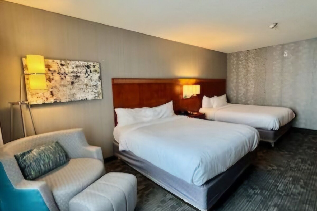 Quarto de hotel com duas camas, um sofá e uma obra de arte na parede.