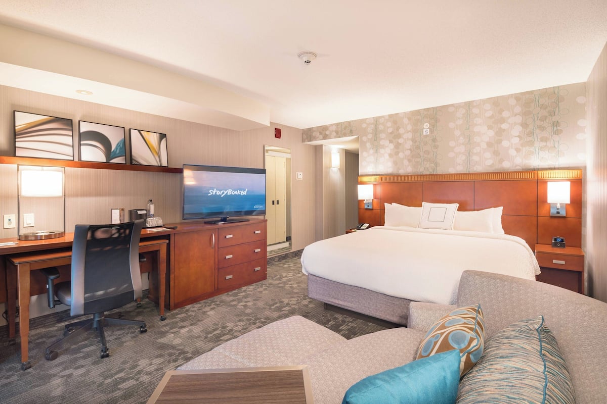 A hotel room with a bed, a desk with a computer, a television, and a sofa.