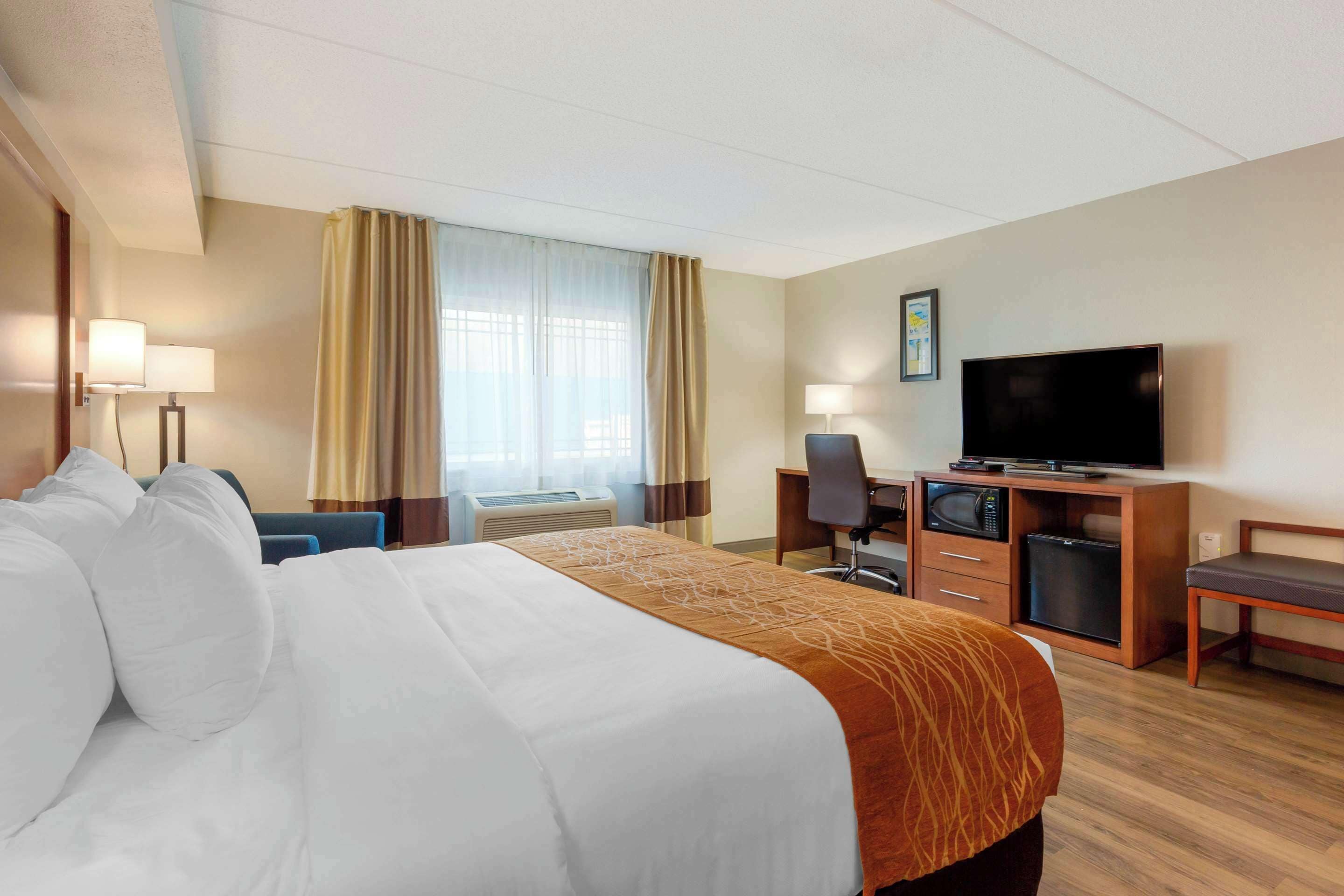 Una habitación de hotel con una cama grande, un escritorio con una computadora, un televisor y un microondas.