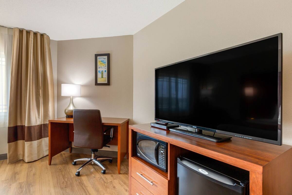 Habitación de hotel con televisión de pantalla plana, escritorio con silla, lámpara, microondas y refrigerador pequeño.