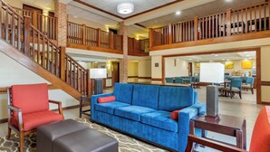 A spacious lobby with a blue sofa, red armchair, and a staircase leading to an upper level.