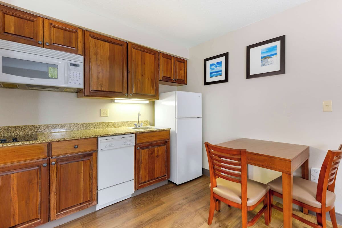 Una cocina con armarios de madera, microondas, lavavajillas, refrigerador y una mesa de comedor con sillas.