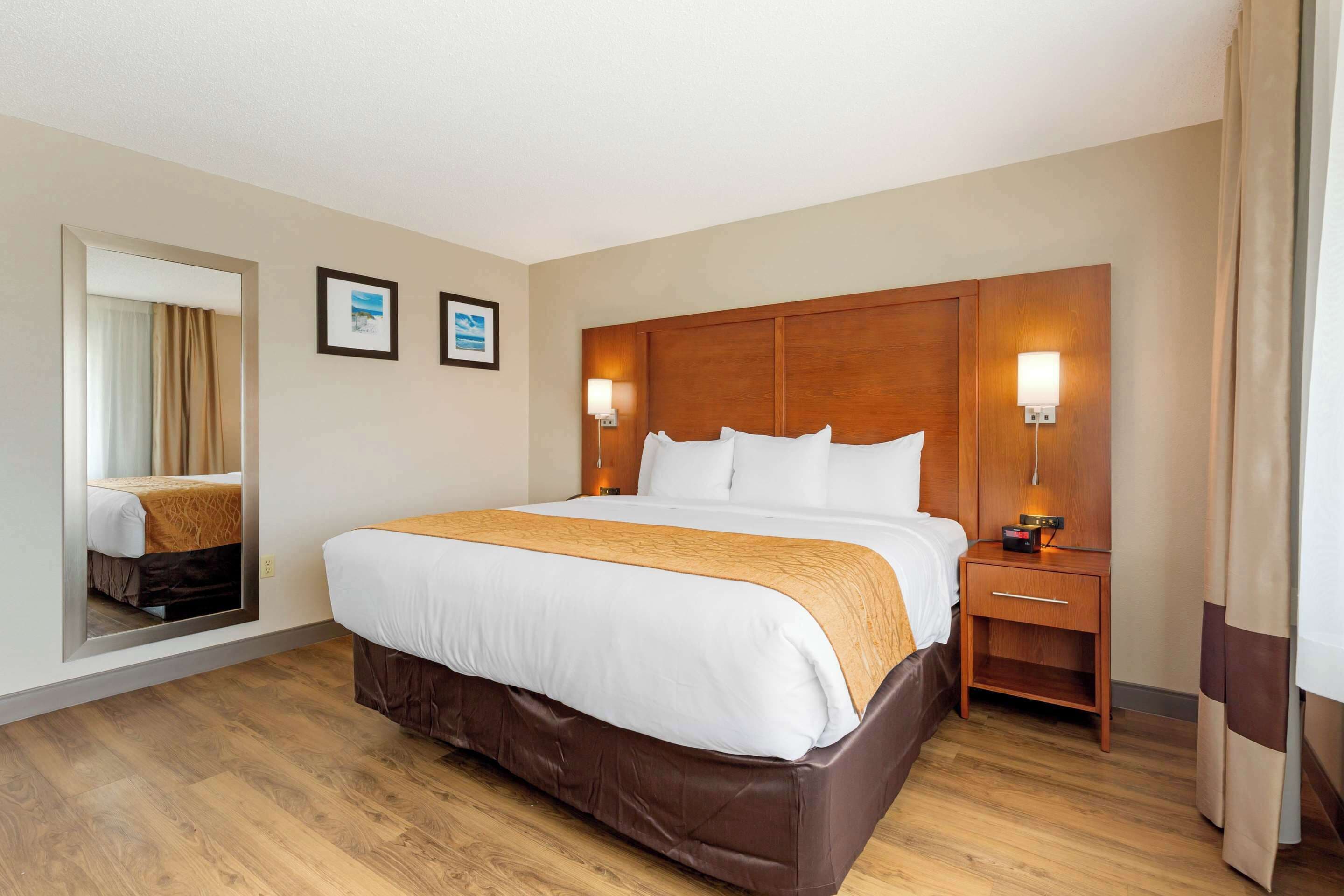 Une chambre d’hôtel avec un grand lit, une tête de lit en bois, des lampes de chevet, une table de chevet et un miroir.