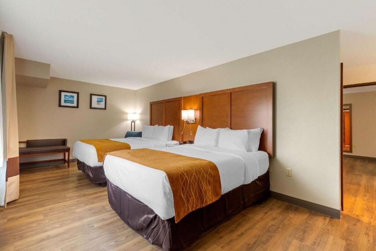 A hotel room with two beds, a bench, and a desk.
