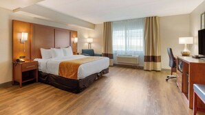 A hotel room with a bed, bedside tables, a desk, a chair, a TV, and a window with curtains.