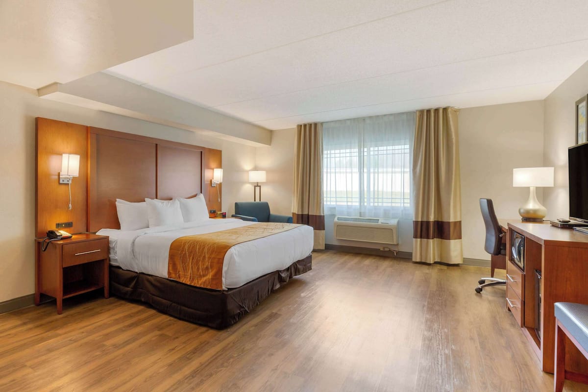 Habitación de hotel con cama, mesitas de noche, escritorio, silla, televisor y ventana con cortinas.