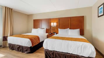 A hotel room with two beds, wooden headboards, a nightstand with a lamp, and a window with curtains.