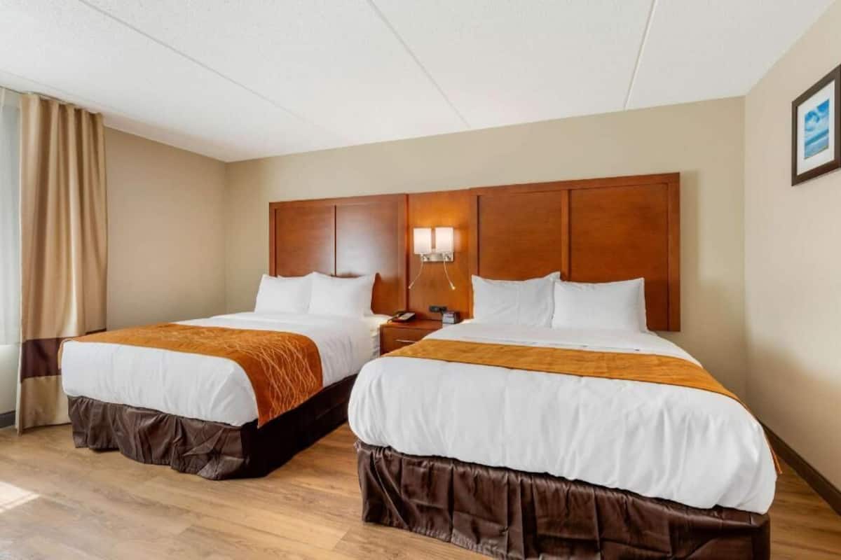 Una habitación de hotel con dos camas, cabecera de madera, mesita de noche y lámpara de pared.