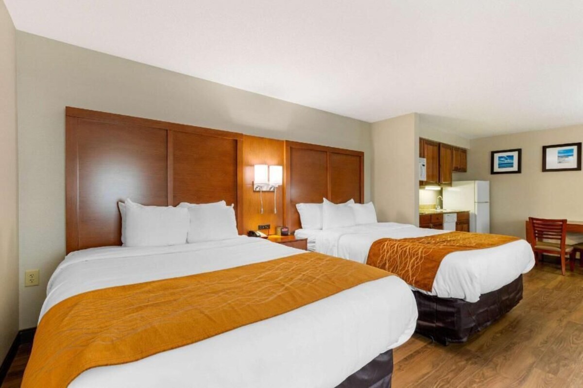A hotel room with two beds, a small kitchenette, a desk, and a chair.