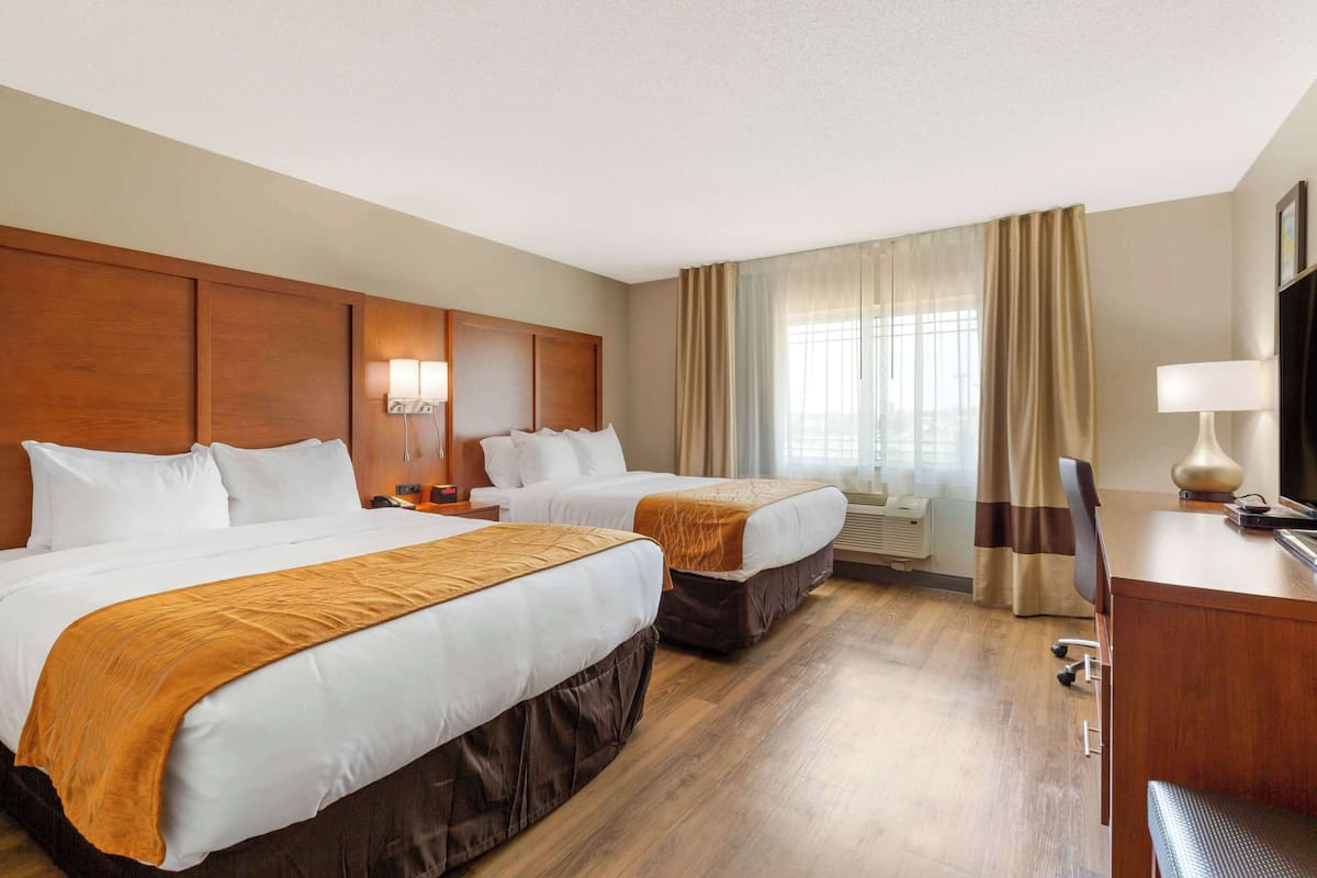 Habitación de hotel con dos camas, un escritorio, una silla, un televisor y un ventanal con cortinas.