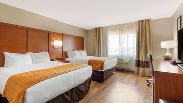 A hotel room with two beds, a desk, a chair, a TV, and a window with curtains.