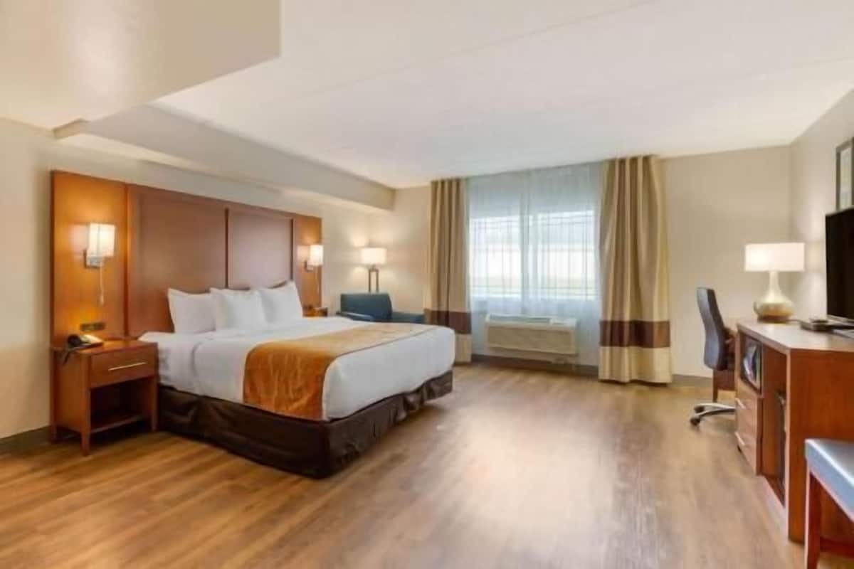 Habitación de hotel con cama, mesitas de noche, escritorio, silla, televisor y ventana con cortinas.