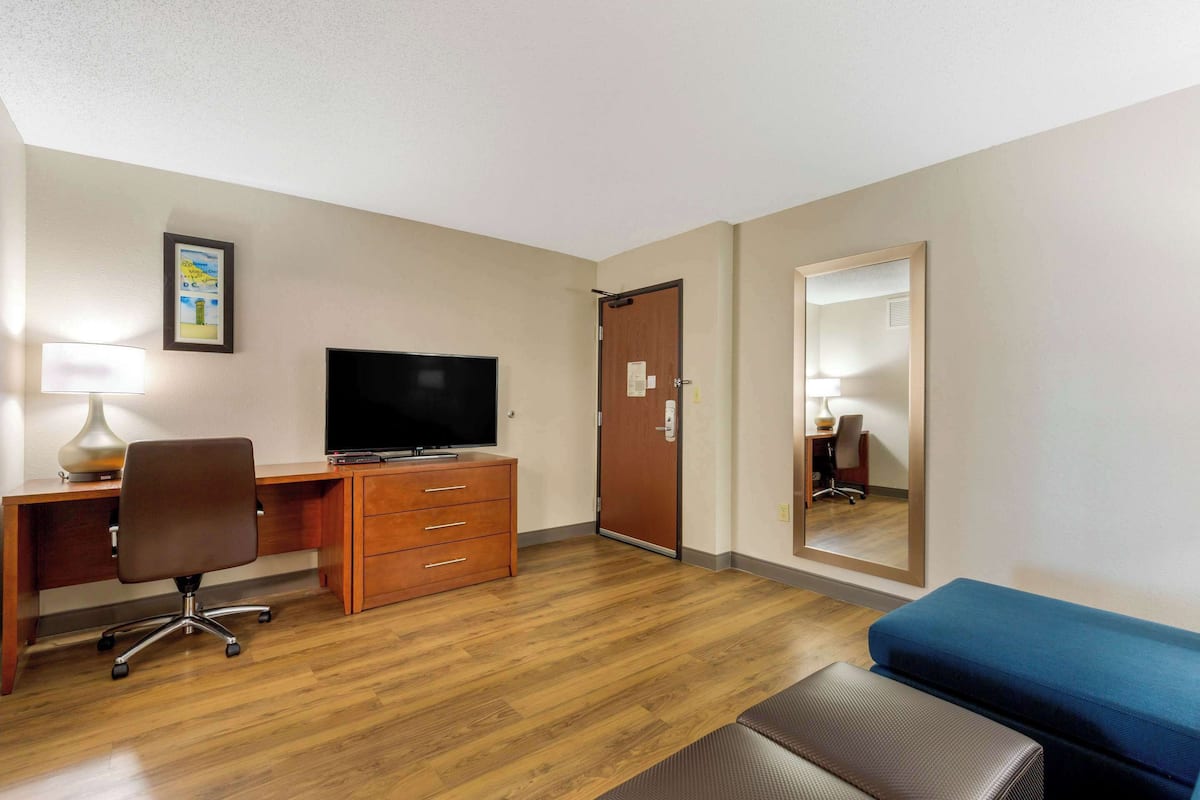 Una habitación de hotel con un escritorio de madera, un televisor, un espejo, un sofá azul y piso de madera.