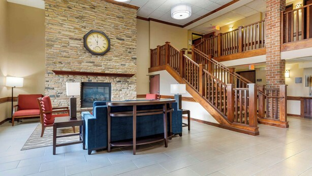 A lobby with a stone wall, a fireplace, a clock, a staircase, and a seating area with a table and chairs.