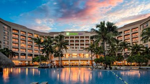 A hotel with a large pool, palm trees, and a sunset sky. - Holiday Inn Resort Sanya Bay by IHG (Sanya)
