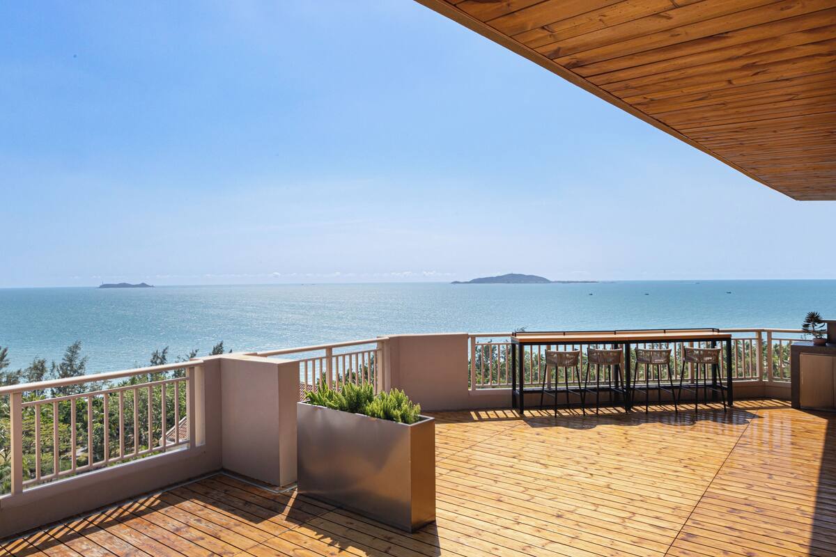 Eine Holzterrasse mit Blick auf das Meer und entfernte Inseln.