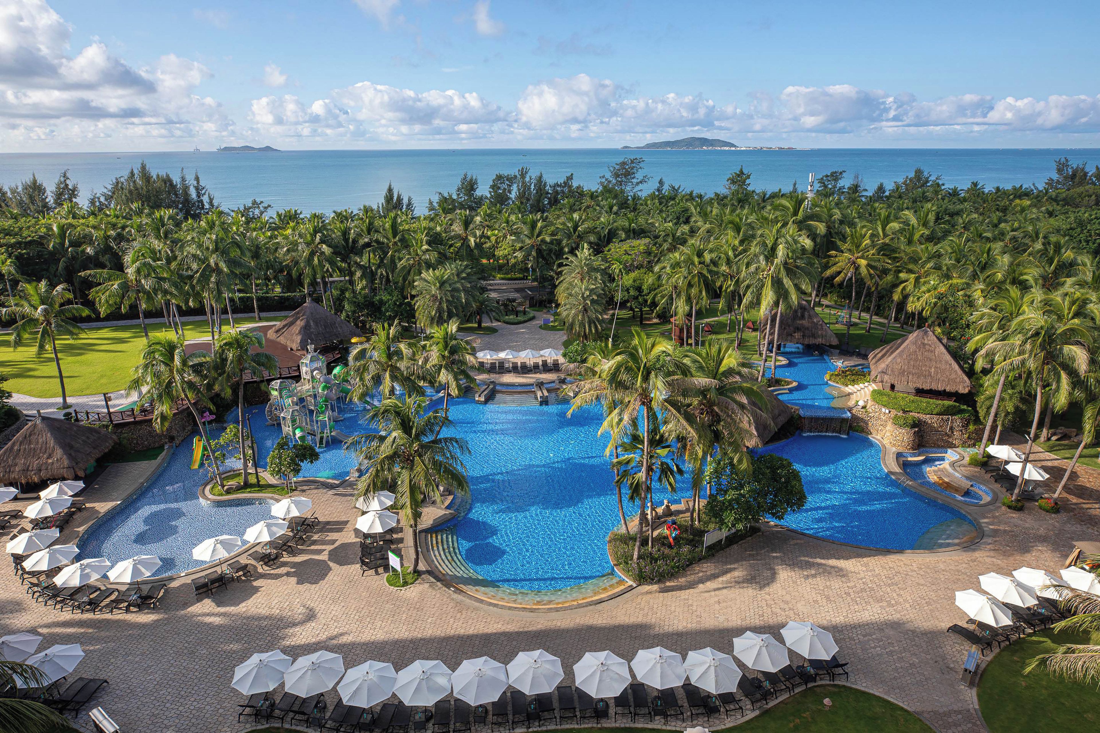 A resort with multiple swimming pools surrounded by palm trees and lounge areas.
