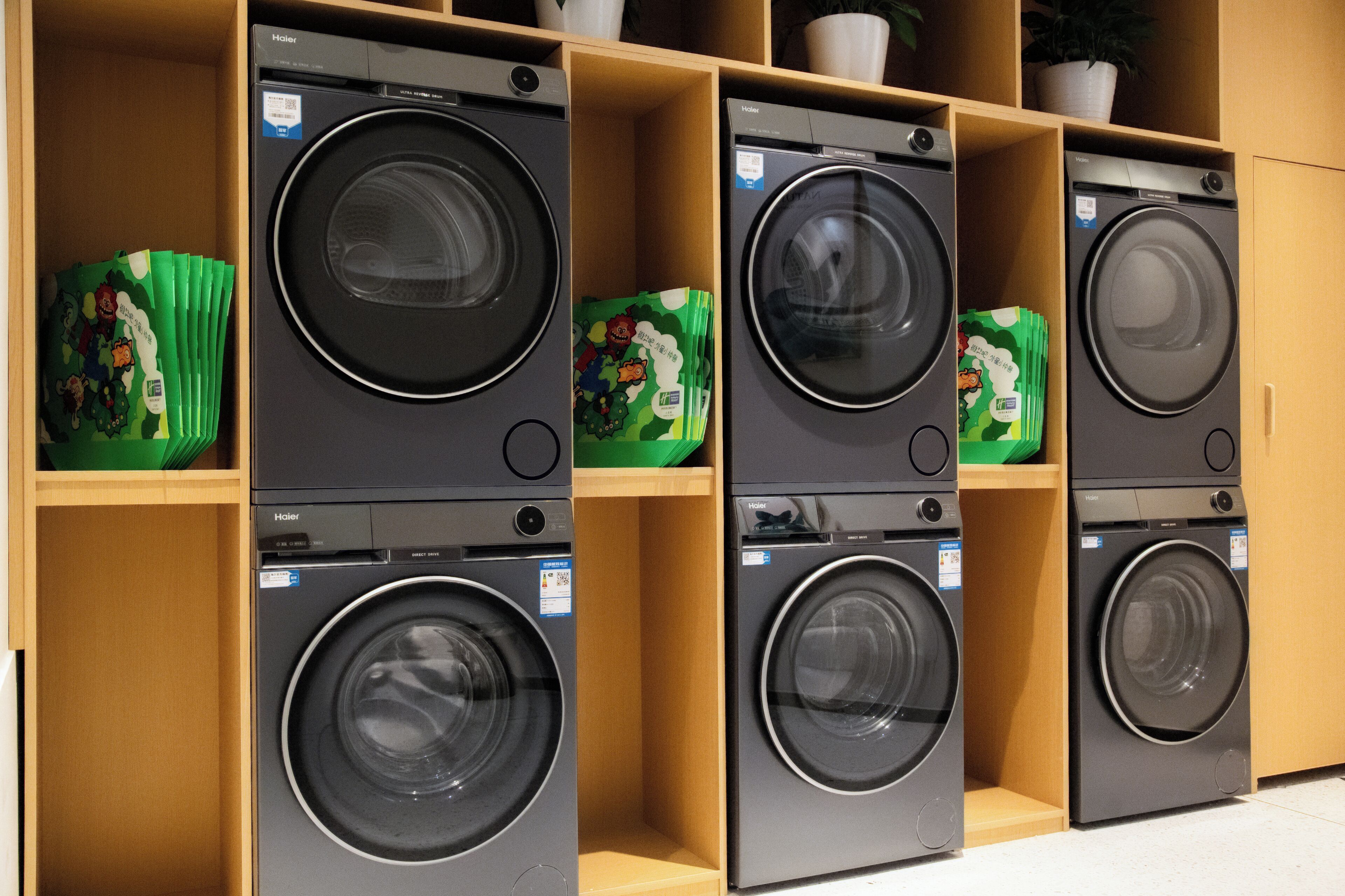 A row of Haier washing machines in a showroom with wooden shelves and green packaging.