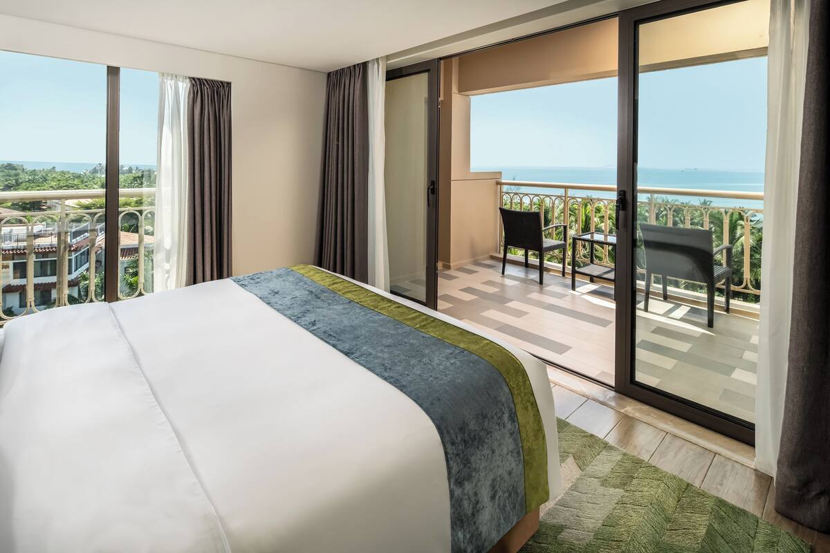 Ein Hotelzimmer mit Bett, einem Balkon mit Meerblick und einer Essecke mit Stühlen.