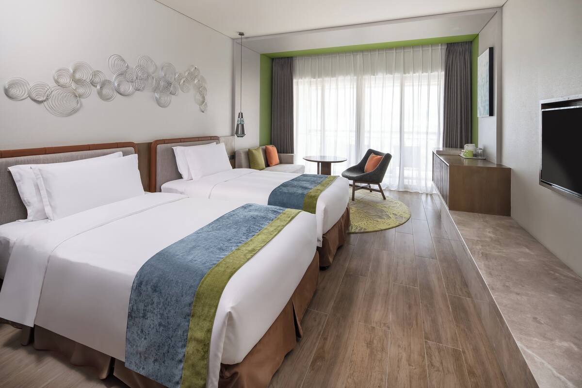 Ein Hotelzimmer mit zwei Betten, einem Schlafsofa, einem Sessel, einem kleinen Tisch und einem Fernseher.
