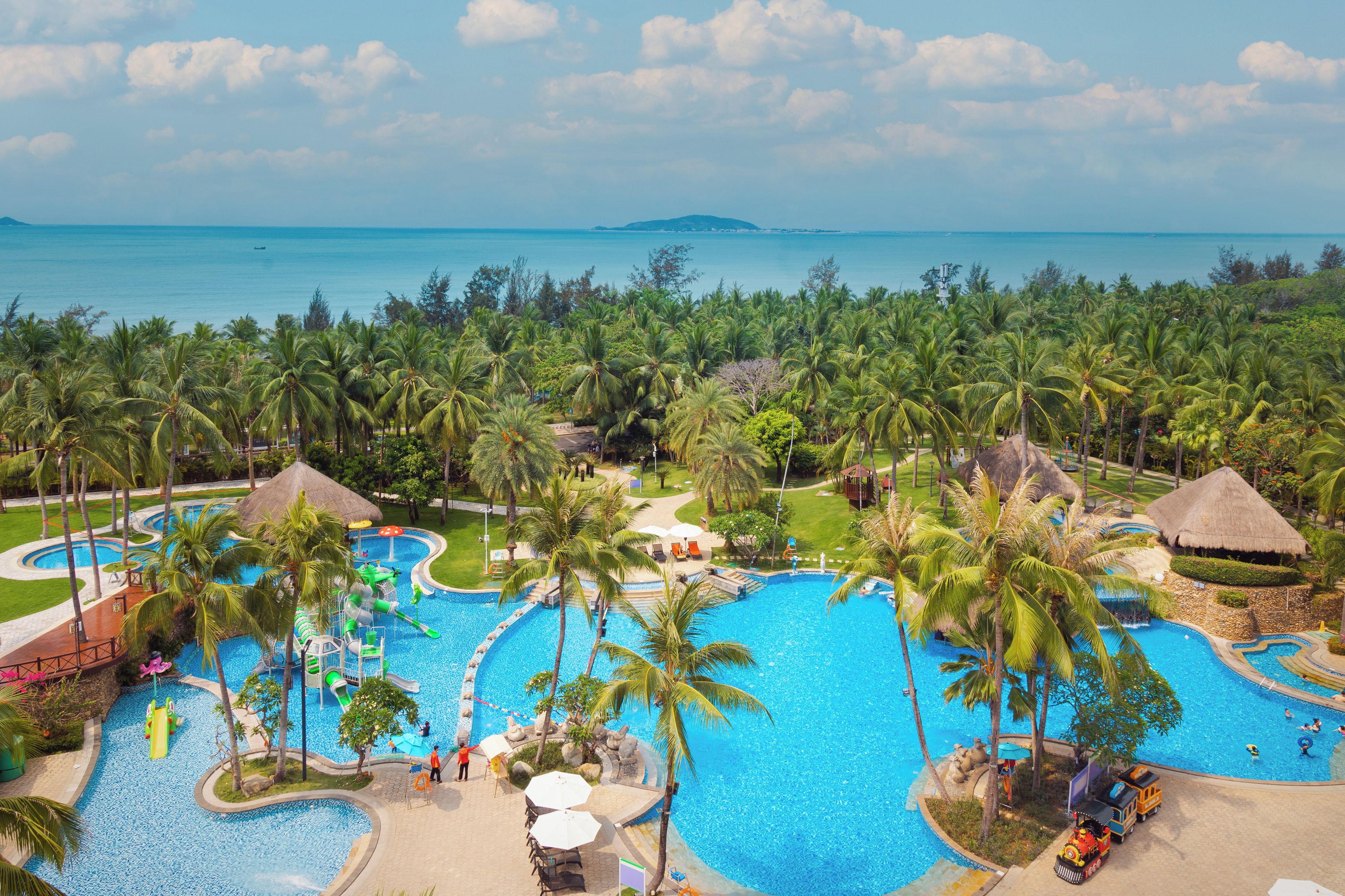 A resort with multiple swimming pools surrounded by palm trees and a view of the ocean.