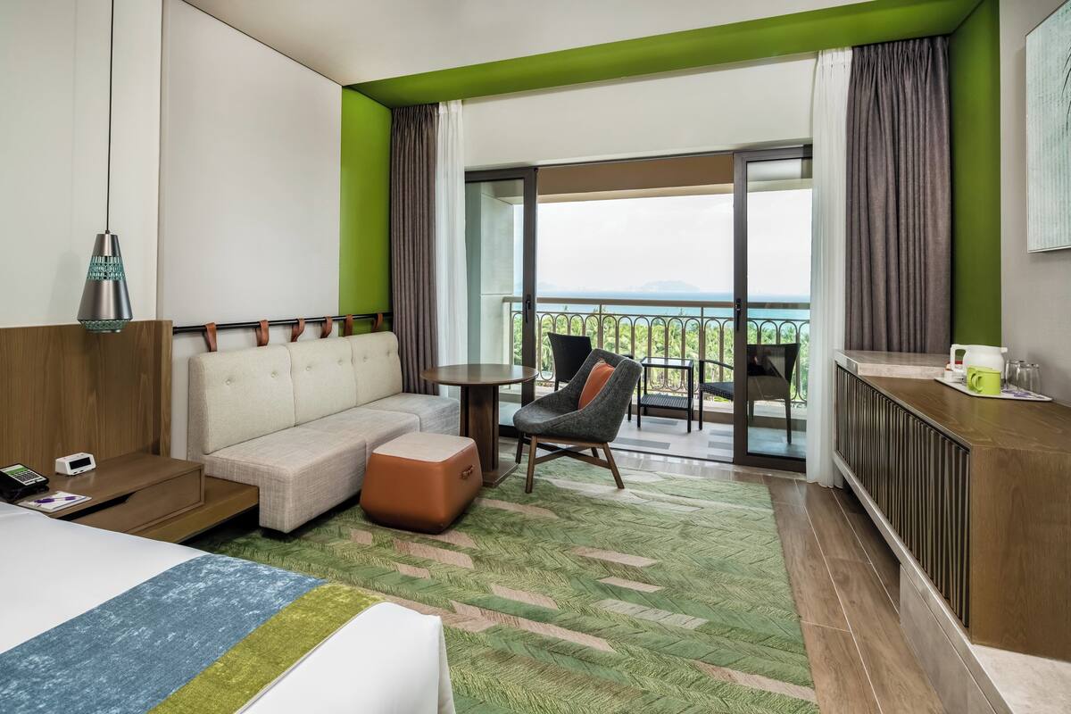 Ein Hotelzimmer mit Bett, Sofa, Sessel, kleinem Tisch und einem Balkon mit Aussicht.