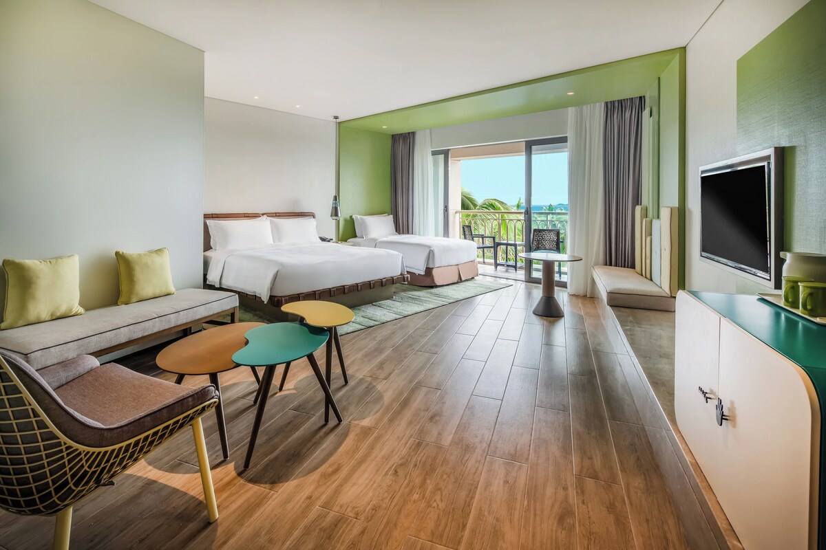 A hotel room with two beds, a sofa, a TV, and a balcony with a view.