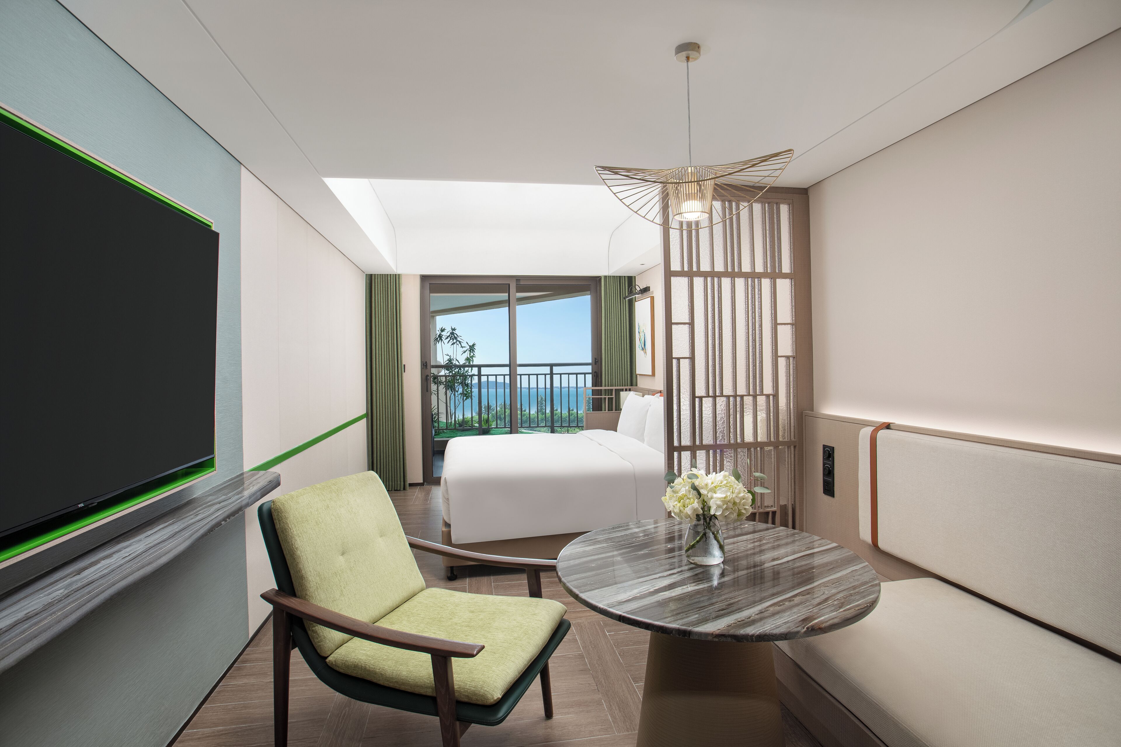 A hotel room with a bed, a chair, a round table with a vase, a TV, and a balcony with a view.